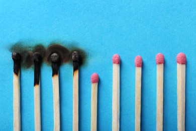 Photo of Burnt and whole matches on light blue background, closeup. Stop destruction by breaking chain reaction concept