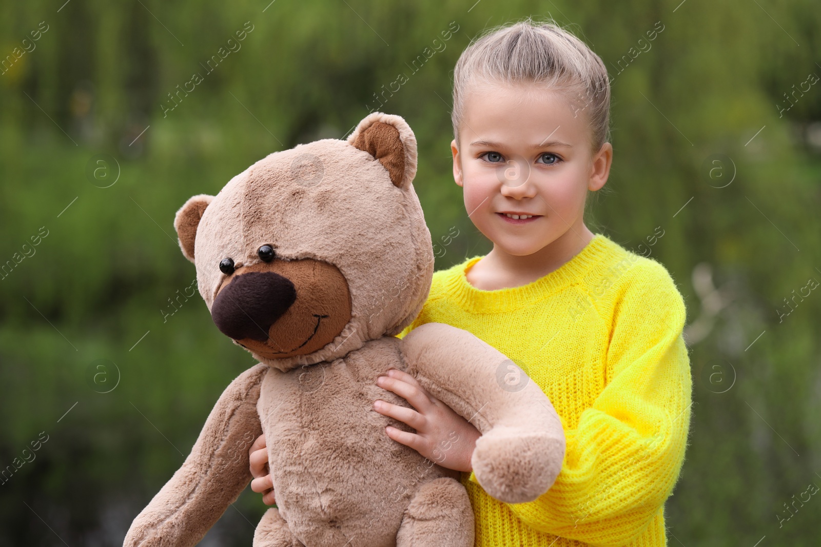 Photo of Cute little girl with teddy bear outdoors