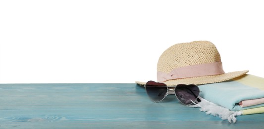 Beach towel, straw hat and heart shaped sunglasses on light blue wooden surface against white background. Space for text