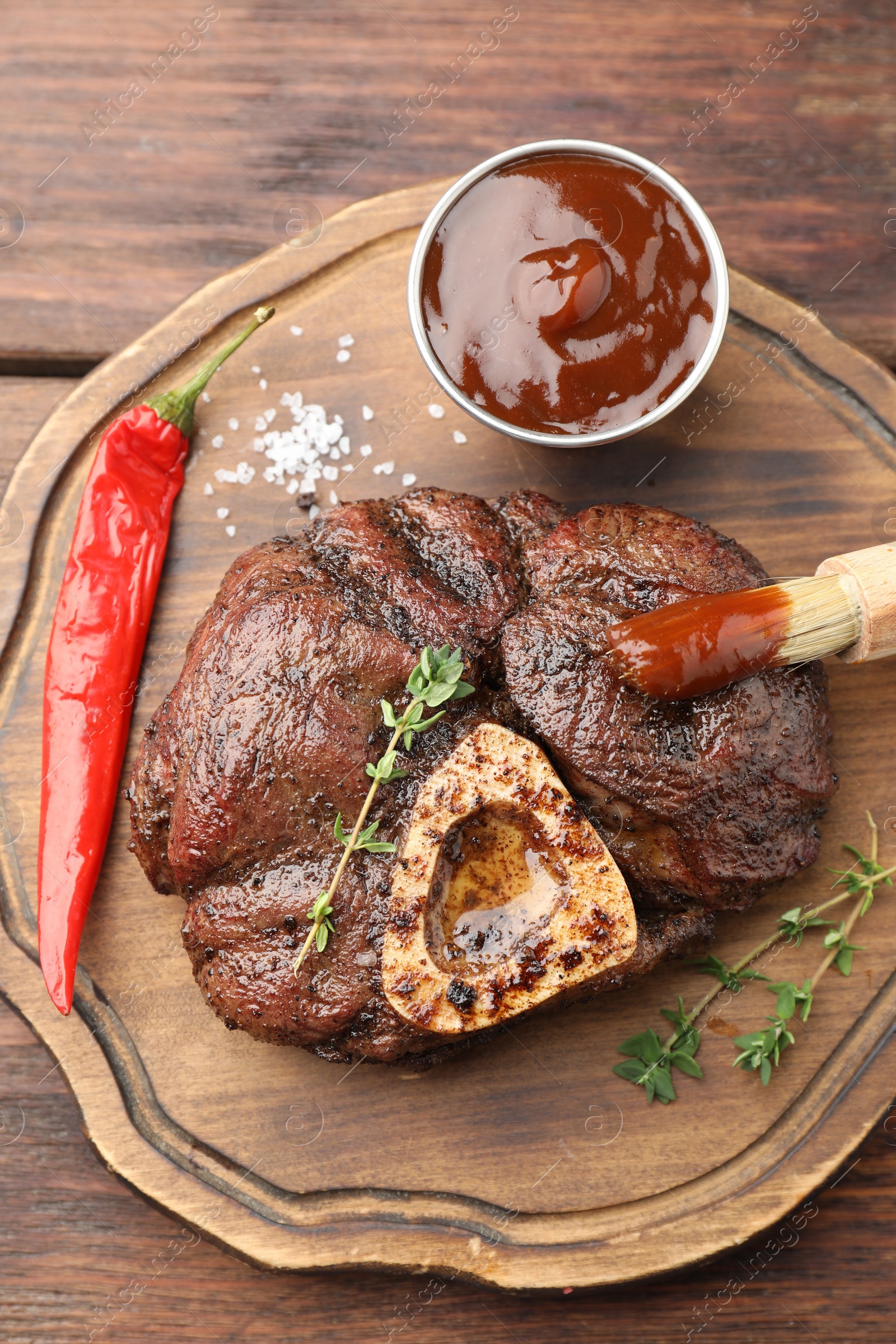 Photo of Delicious roasted beef meat served with sauce and spices on wooden table, top view