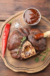 Delicious roasted beef meat served with sauce and spices on wooden table, top view