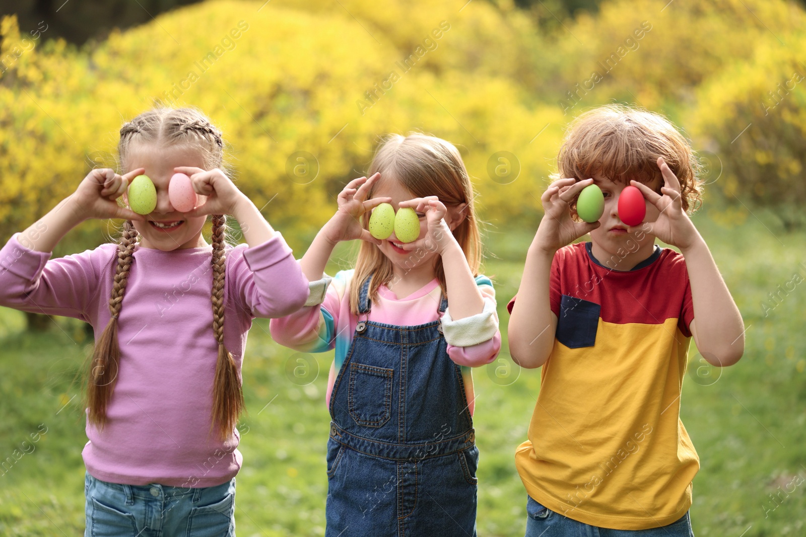 Photo of Easter celebration. Little children covering eyes with painted eggs outdoors