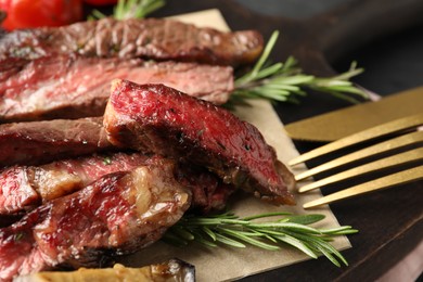 Photo of Delicious grilled beef with rosemary and cutlery on table, closeup
