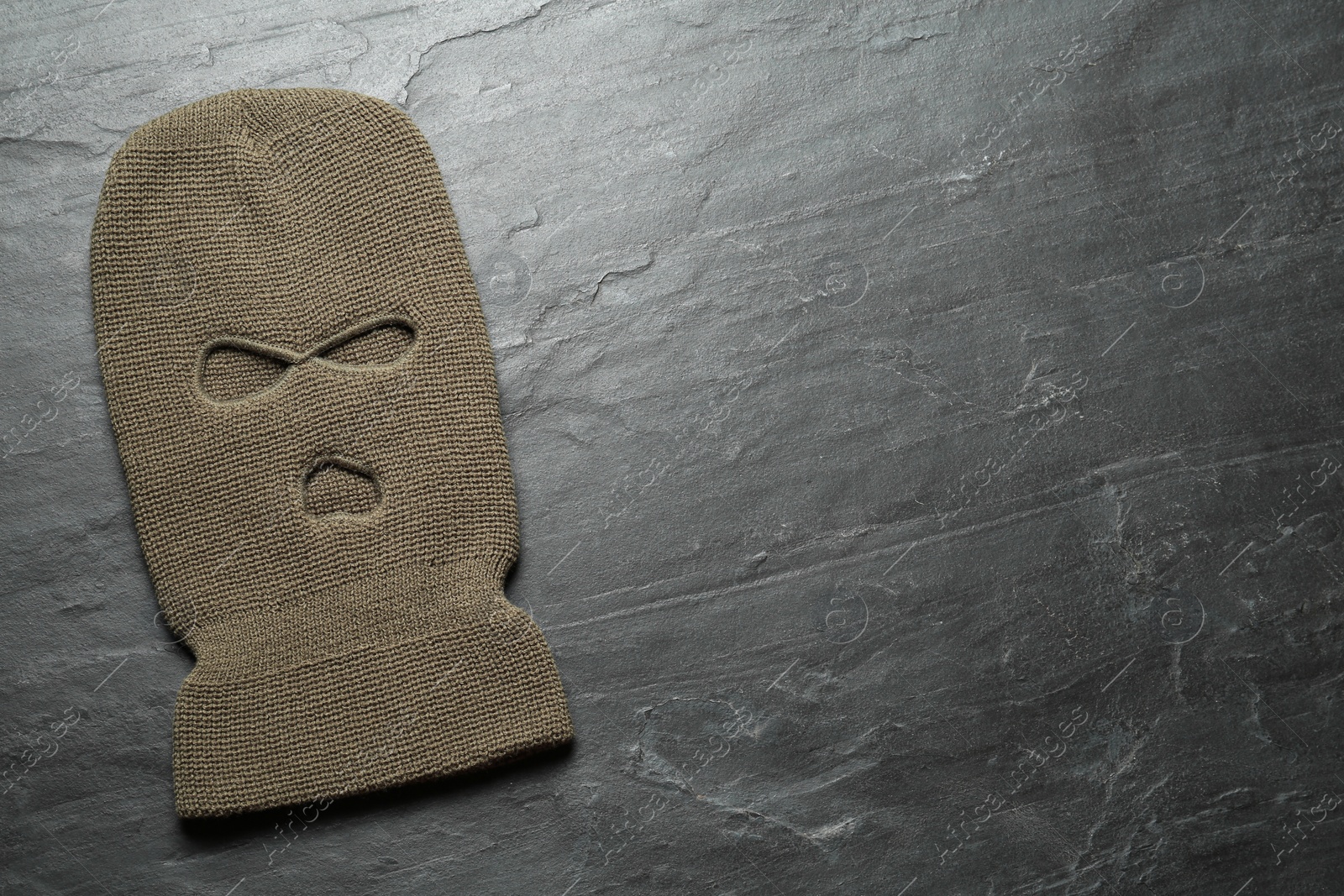 Photo of Beige knitted balaclava on black table, top view. Space for text