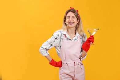Young housewife with glass of martini on yellow background. Space for text