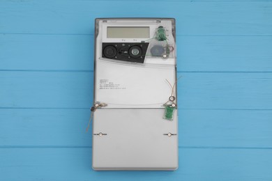 Photo of Electric meter on light blue wooden background, top view. Measuring device