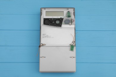 Electric meter on light blue wooden background, top view. Measuring device