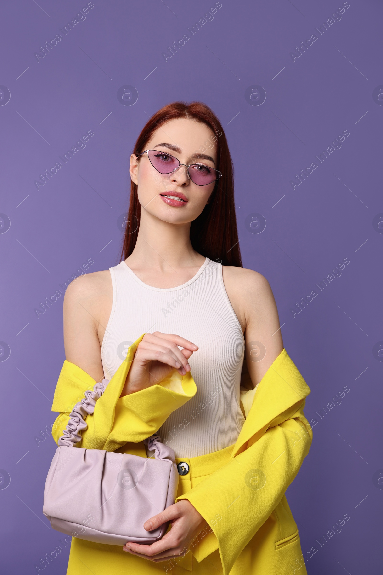 Photo of Stylish woman with red dyed hair and bag on purple background