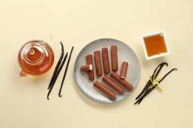 Photo of Glazed curd cheese bars, vanilla pods and tea on beige background, flat lay