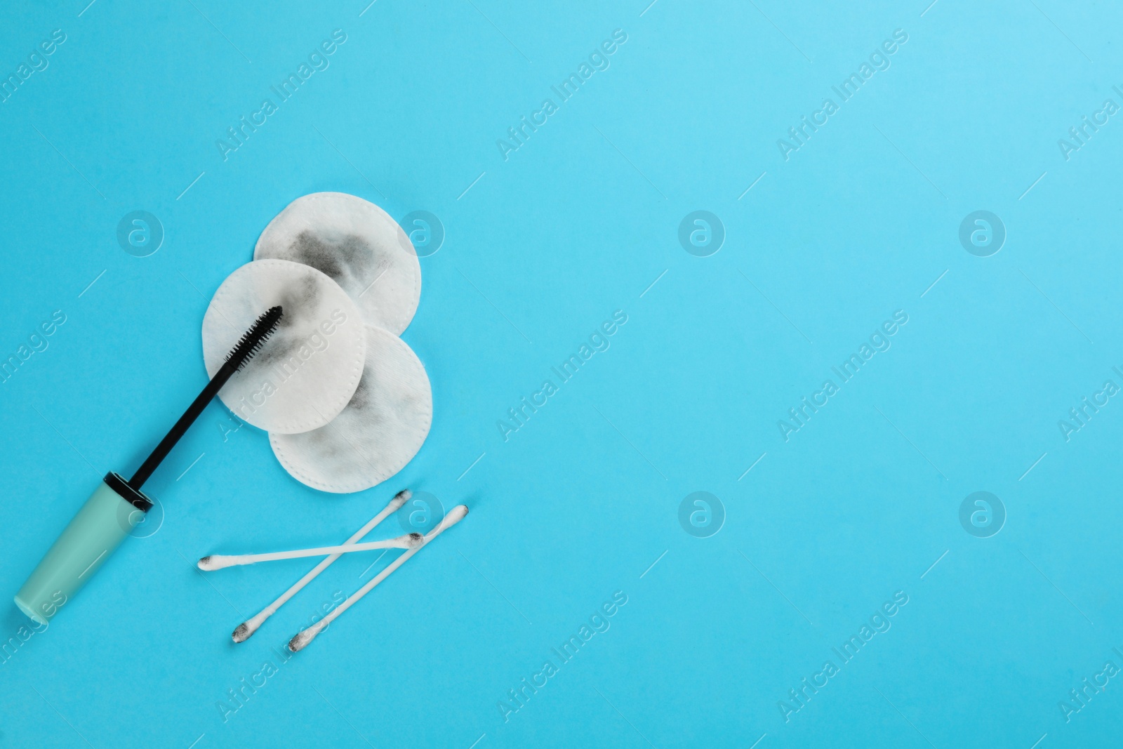 Photo of Dirty cotton pads, swabs with mascara on turquoise background, flat lay. Space for text