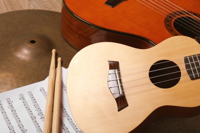 Photo of Ukulele, acoustic guitar, drumsticks, cymbal and note sheets on wooden background, closeup. Musical instruments