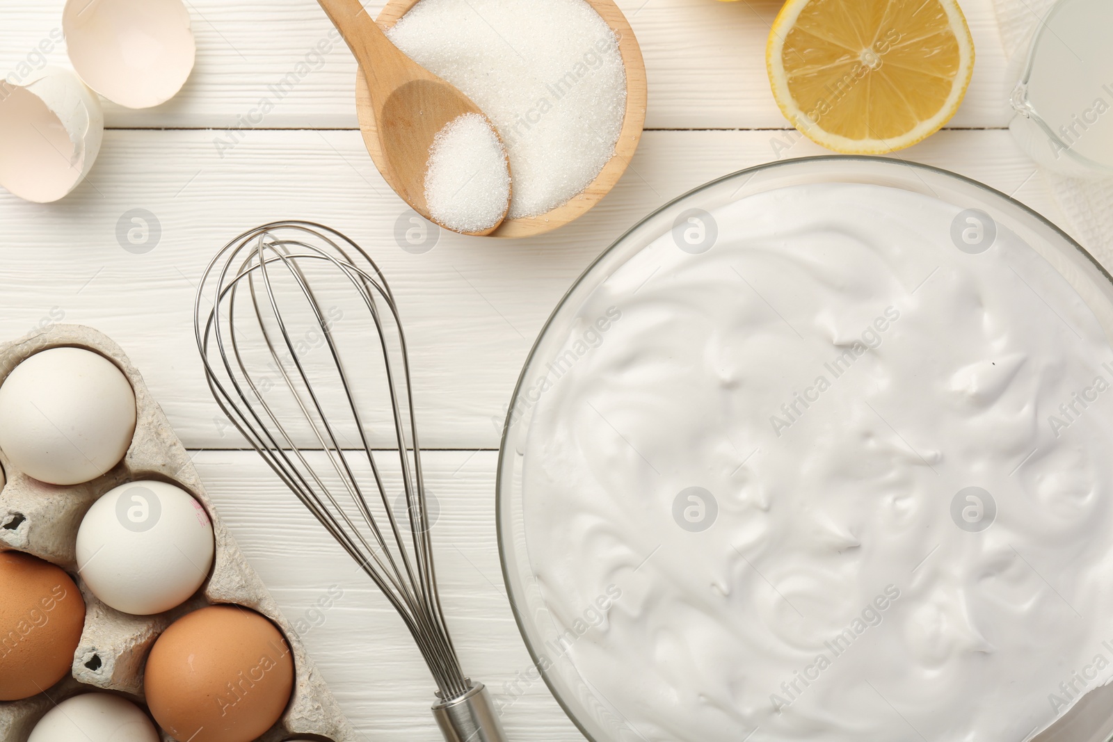 Photo of Bowl with whipped cream, whisk and ingredients on white wooden table, flat lay