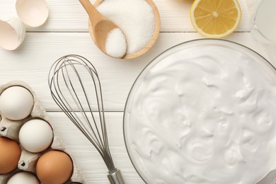 Photo of Bowl with whipped cream, whisk and ingredients on white wooden table, flat lay