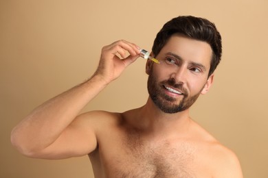 Smiling man applying cosmetic serum onto his face on beige background
