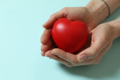 Photo of Woman holding red decorative heart on light blue background, closeup. Space for text