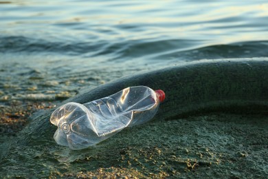 Photo of Used plastic bottle and tire near water at beach. Environment pollution