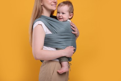 Mother holding her child in baby wrap on orange background, closeup