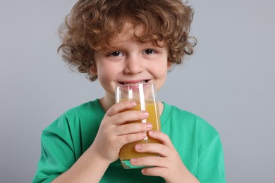 Photo of Cute little boy with glass of fresh juice on light gray background