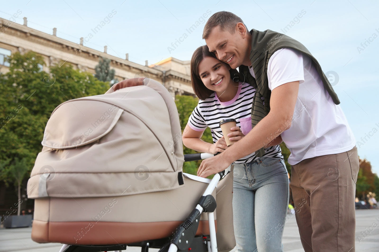 Photo of Happy parents walking with their baby in stroller outdoors