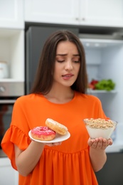 Woman choosing between healthy breakfast and doughnuts in kitchen, focus on food