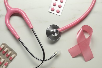 Photo of Pink ribbon, stethoscope and pills on white marble table, flat lay. Breast cancer awareness