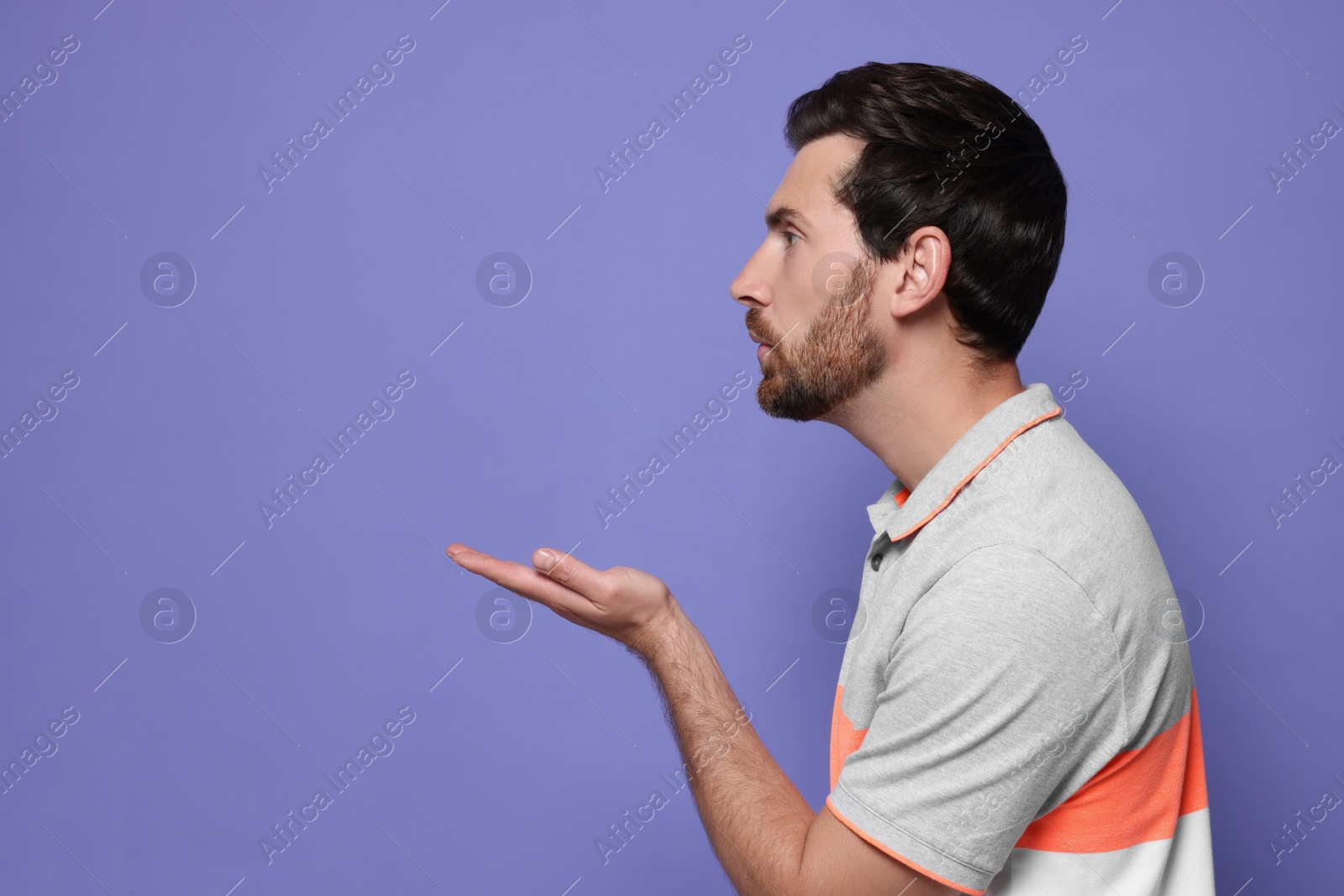 Photo of Handsome man blowing kiss on violet background. Space for text