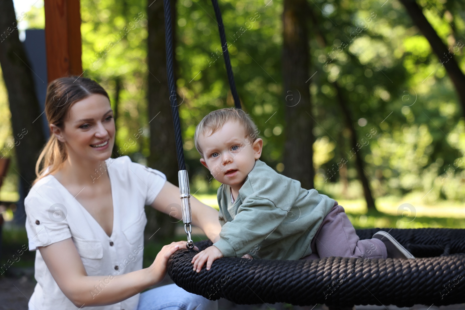 Photo of Happy nanny and cute little boy on swing outdoors