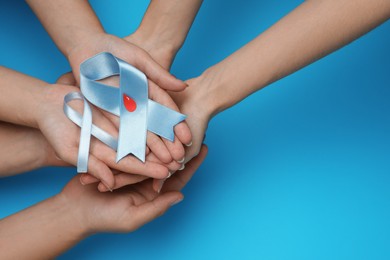 Photo of People holding light blue ribbons with paper blood drop on color background, top view and space for text. Diabetes awareness