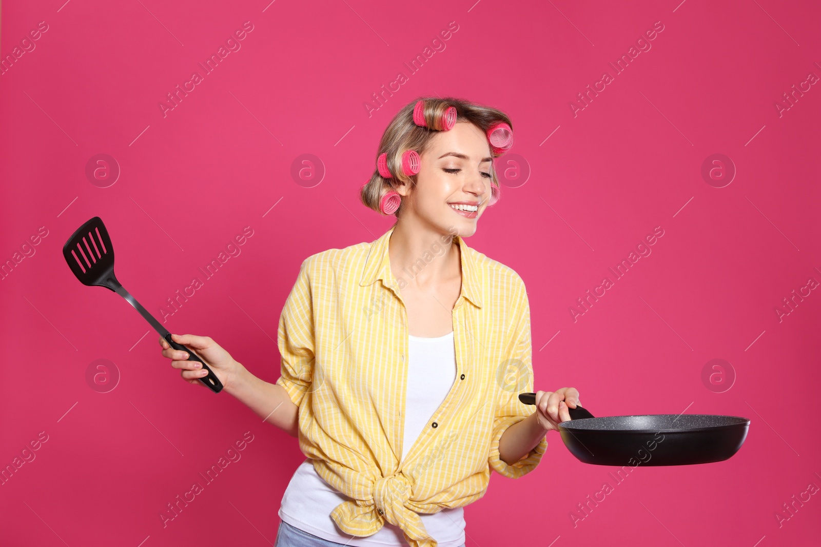 Photo of Young housewife with frying pan and spatula on pink background