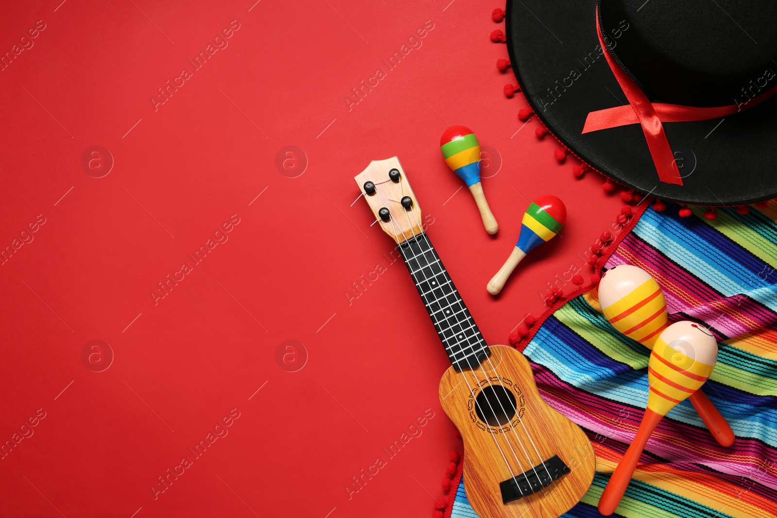 Photo of Mexican sombrero hat, maracas, guitar and colorful poncho on red background, flat lay. Space for text