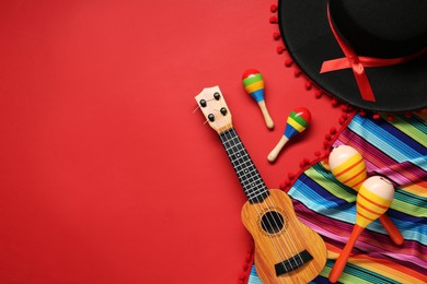Photo of Mexican sombrero hat, maracas, guitar and colorful poncho on red background, flat lay. Space for text