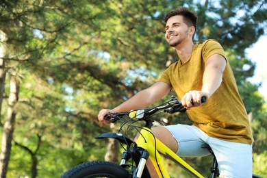 Handsome young man with bicycle in park, low angle view