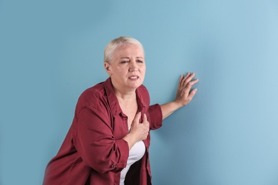 Mature woman having heart attack on color background