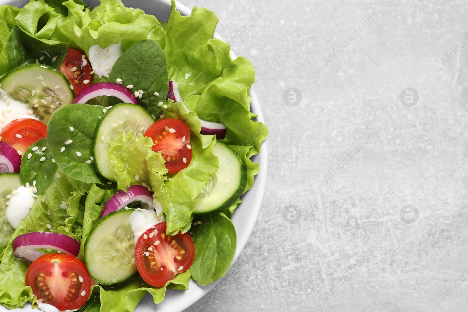 Photo of Delicious salad in bowl on light grey table, top view. Space for text