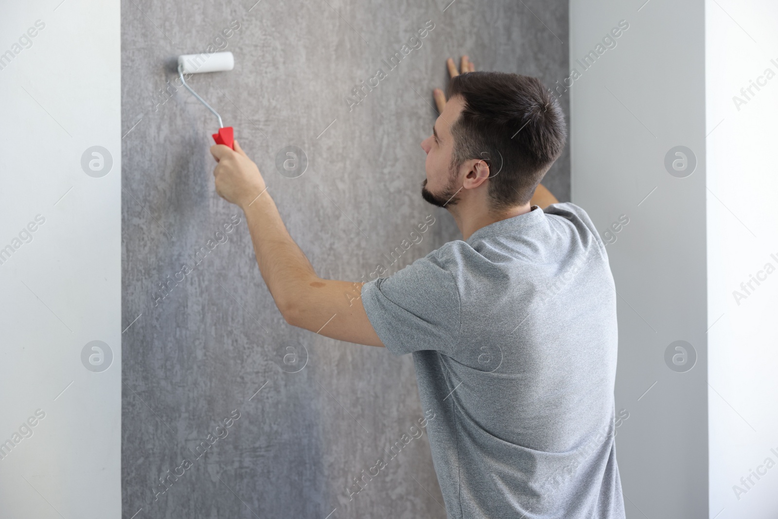 Photo of Man hanging stylish gray wallpaper in room