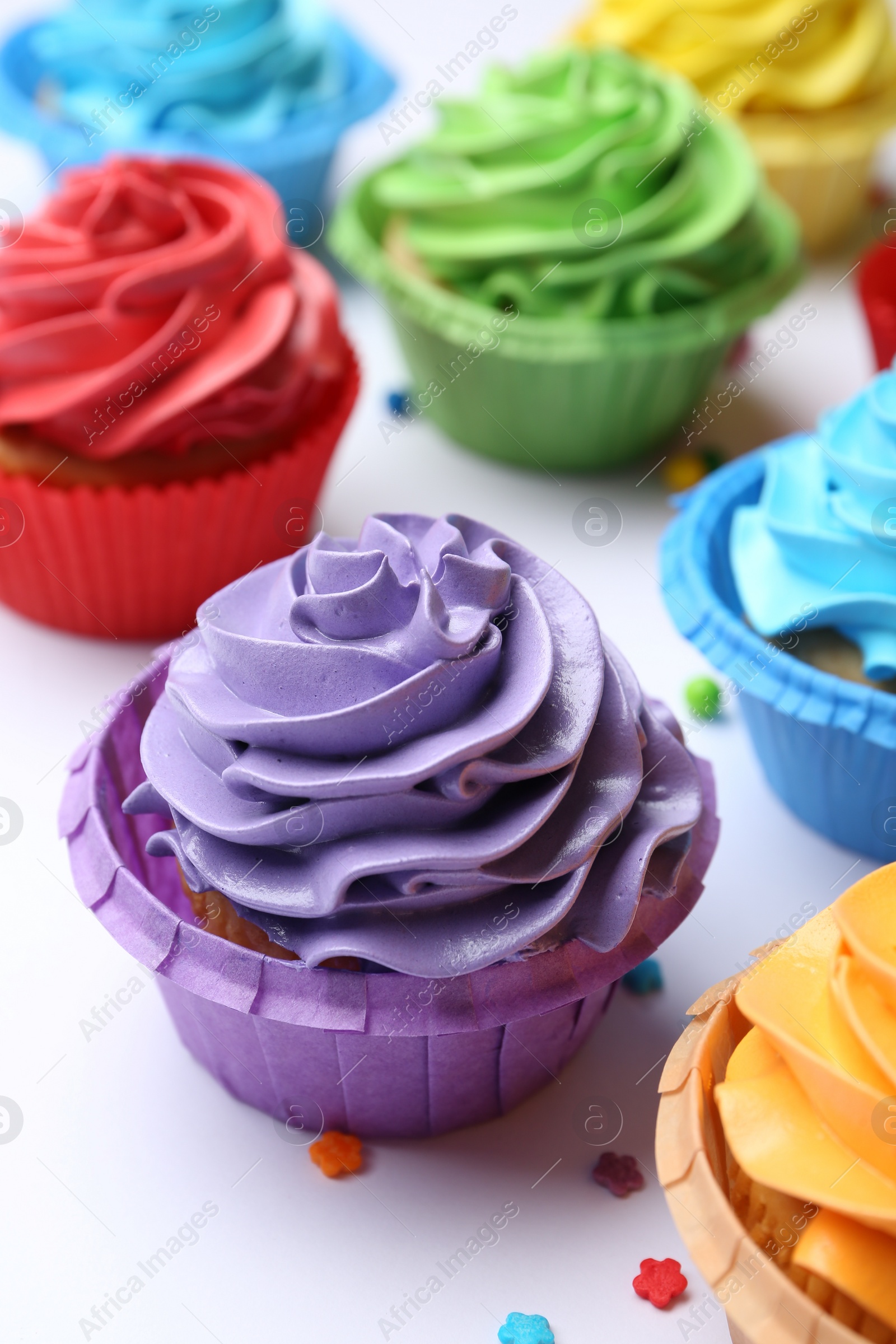 Photo of Many tasty cupcakes with bright cream and sprinkles on white background, closeup