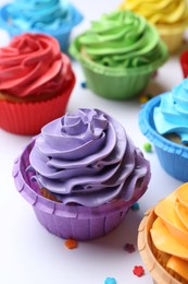 Many tasty cupcakes with bright cream and sprinkles on white background, closeup