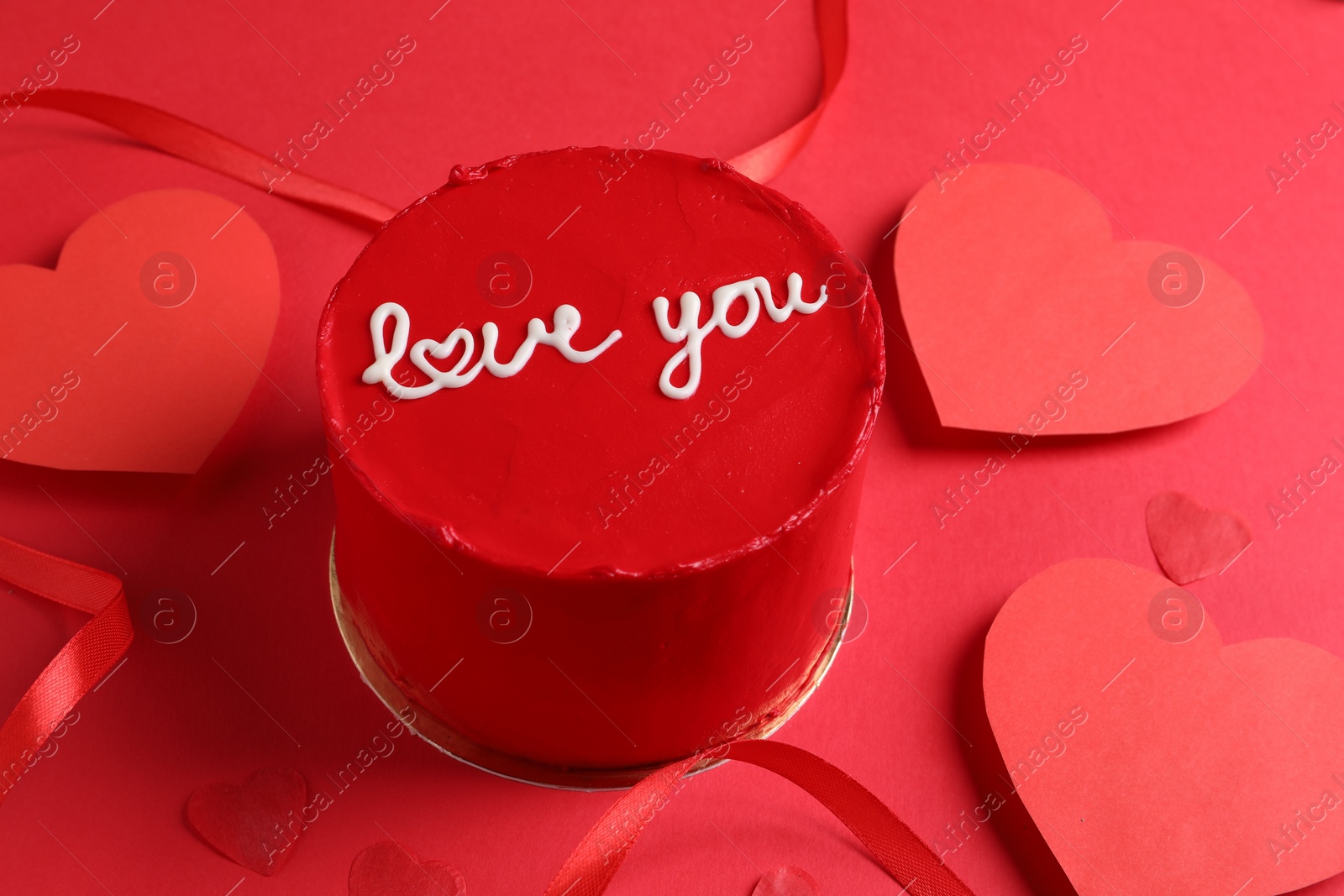 Photo of Bento cake with text Love You, ribbon and paper hearts on red table. St. Valentine's day surprise