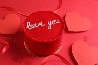 Photo of Bento cake with text Love You, ribbon and paper hearts on red table. St. Valentine's day surprise