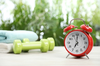 Photo of Alarm clock on white wooden table outdoors, space for text. Morning exercise