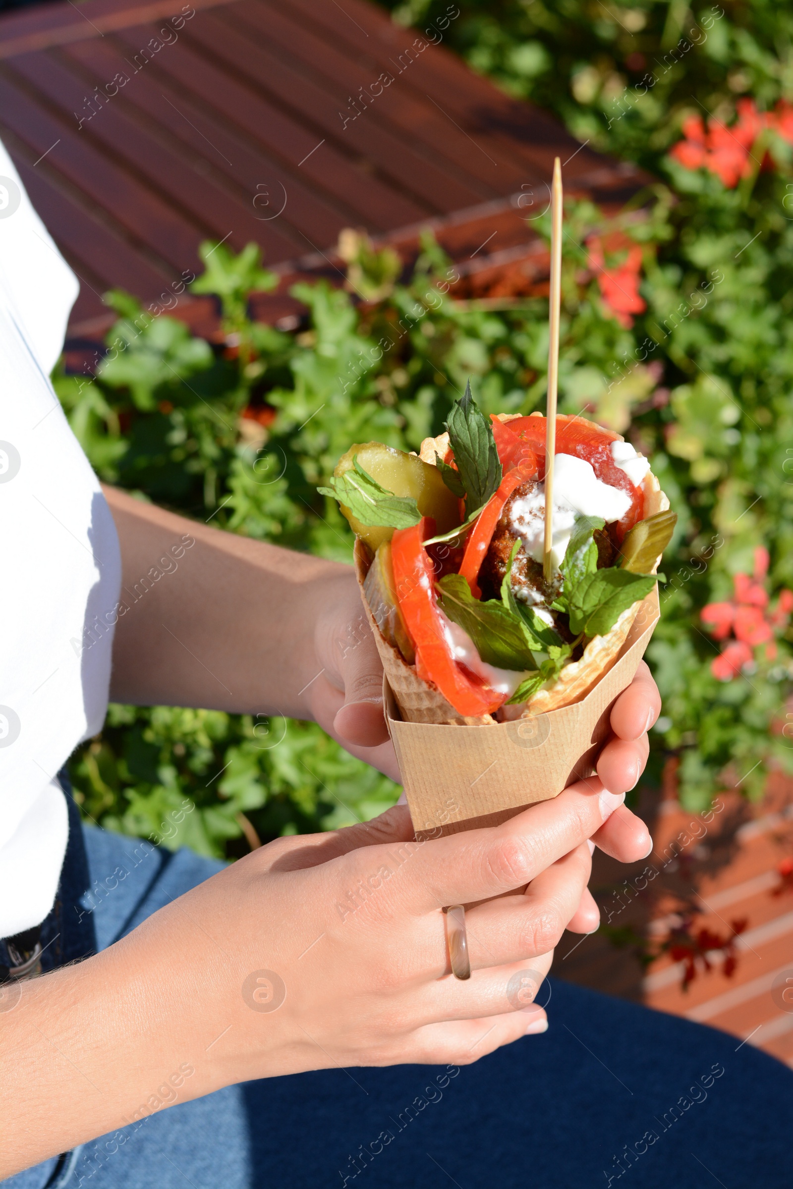 Photo of Woman holding wafer with falafel and vegetables outdoors, closeup. Street food