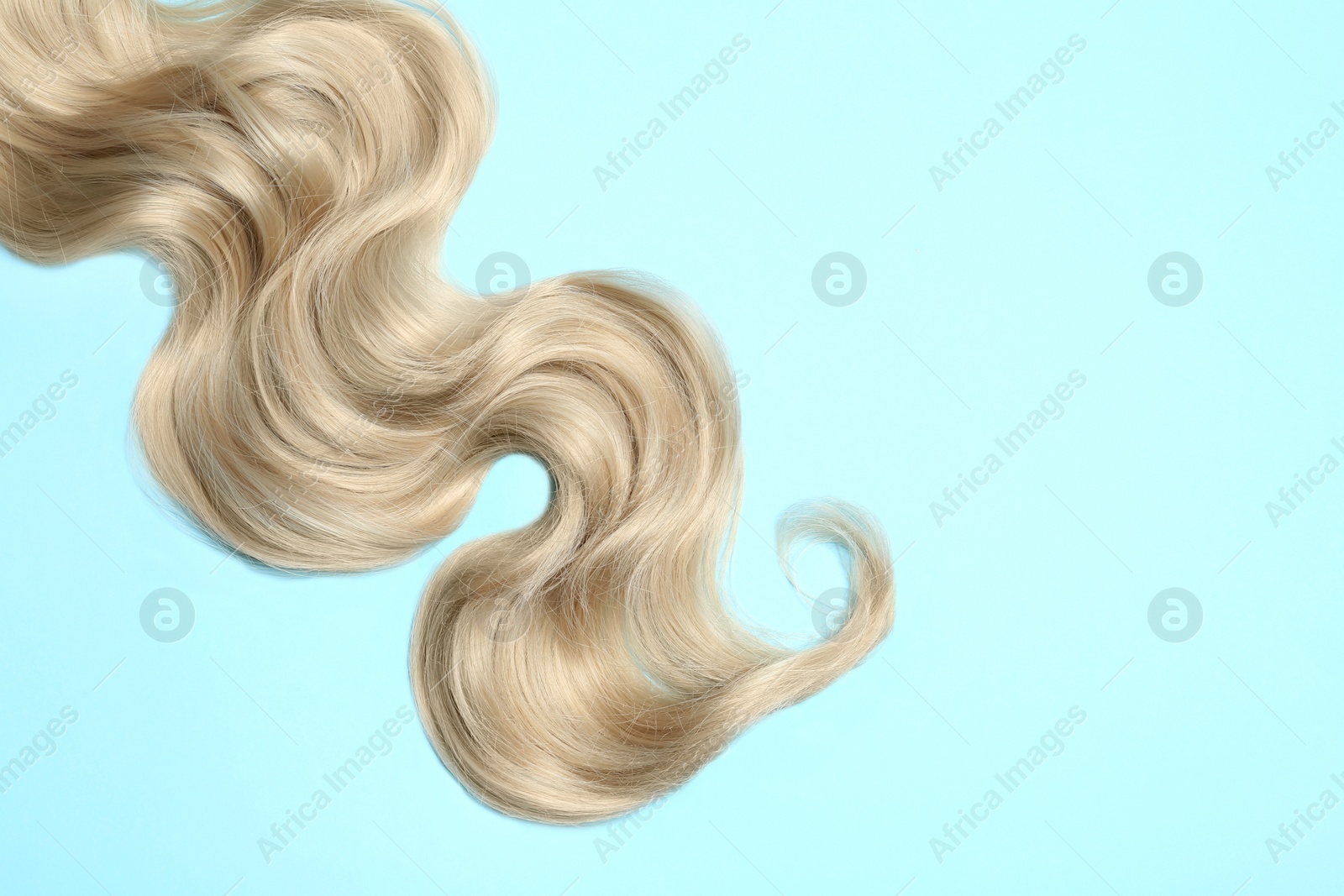 Photo of Lock of blonde wavy hair on color background, top view. Space for text