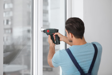 Construction worker repairing plastic window with electric screwdriver indoors