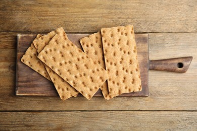 Photo of Board with fresh rye crispbreads on wooden table, top view