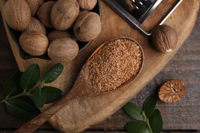 Photo of Spoon with grated nutmeg, seeds and green branches on wooden table, flat lay