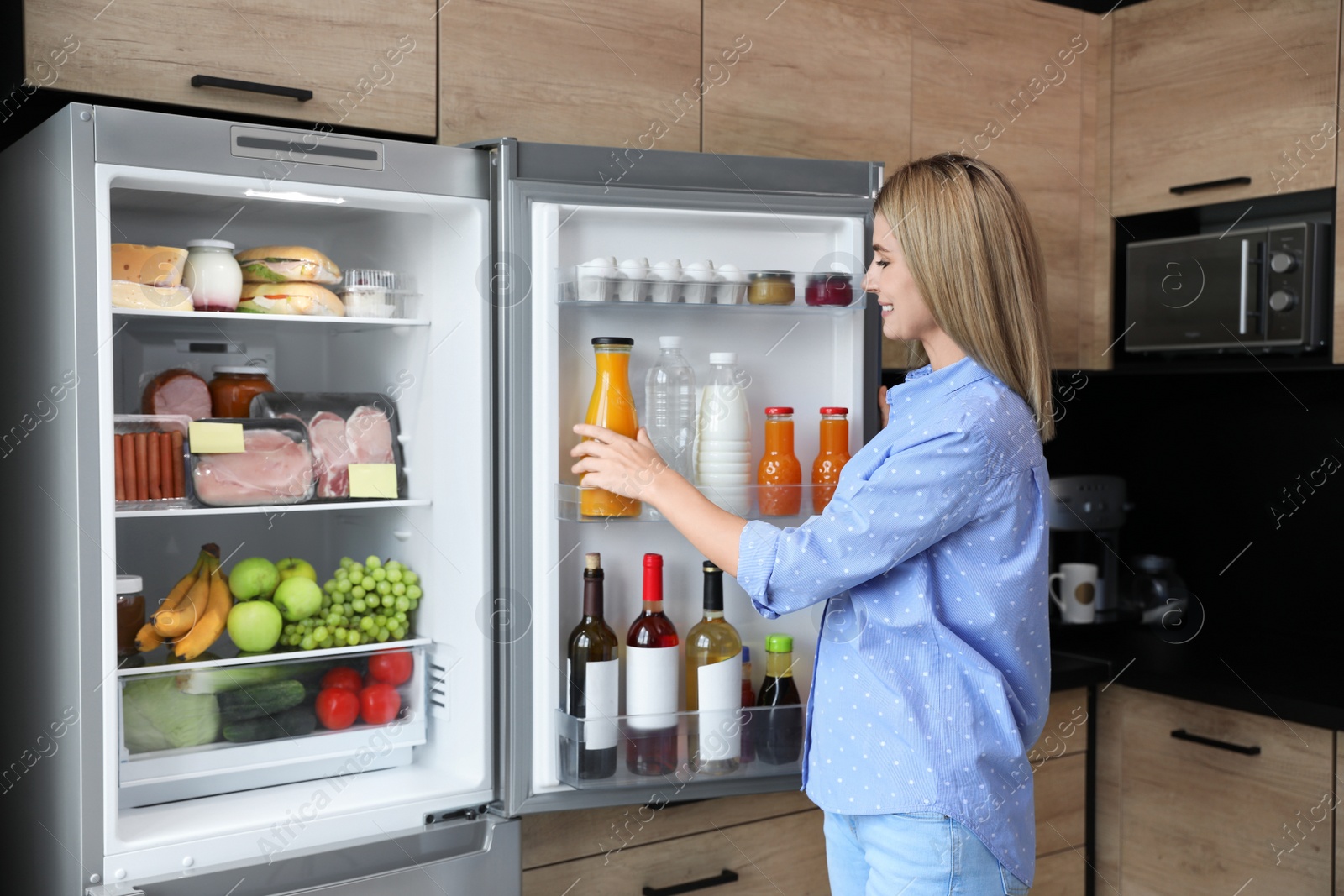 Photo of Woman taking bottle with juice out of refrigerator in kitchen