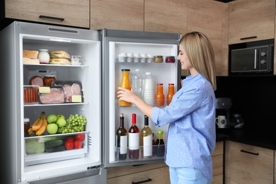 Woman taking bottle with juice out of refrigerator in kitchen