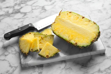 Photo of Board with fresh sliced pineapple and knife on marble table