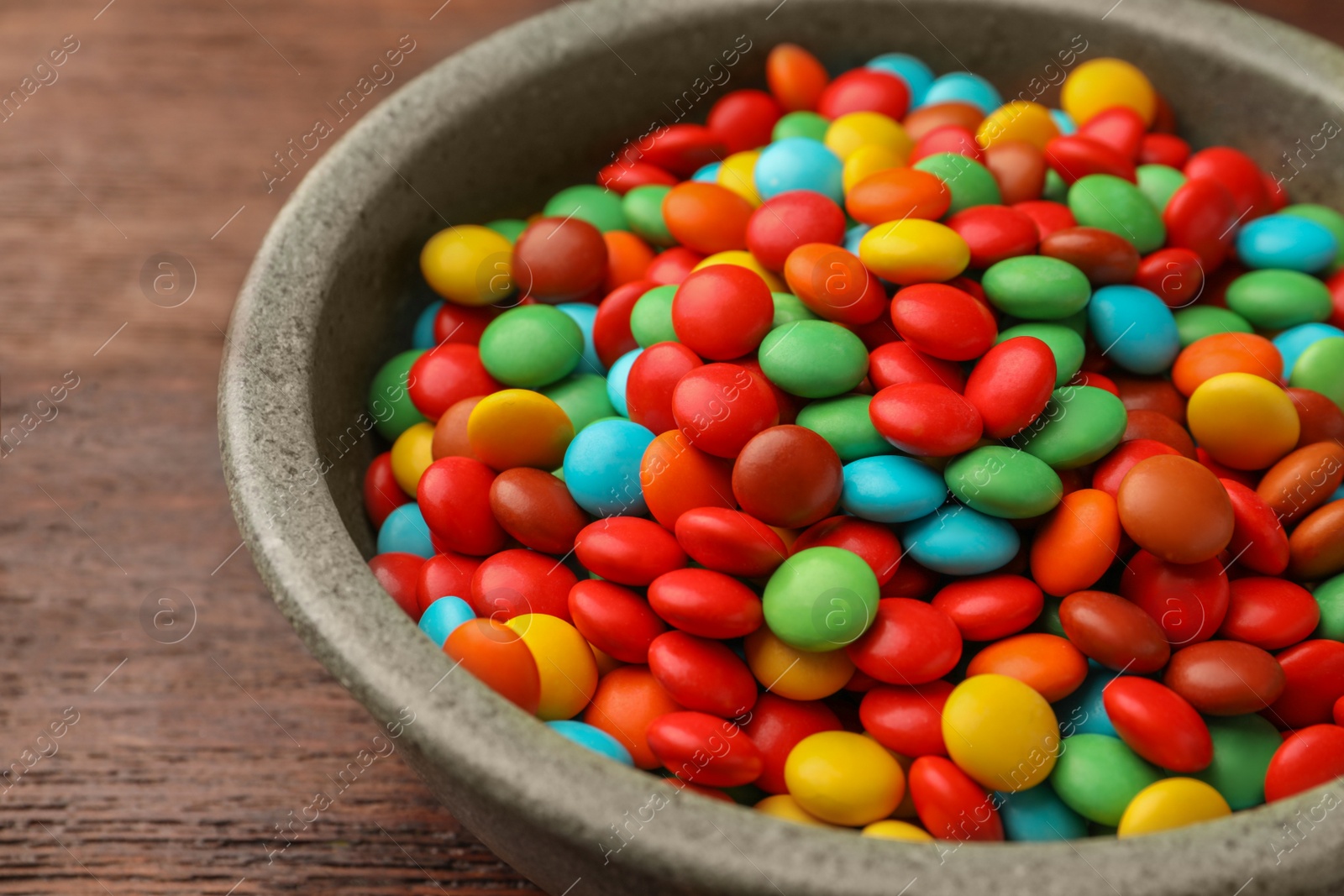 Photo of Bowl with tasty colorful candies on wooden table, closeup