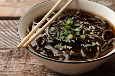 Photo of Tasty soup with buckwheat noodles (soba), onion in bowl and chopsticks on wooden table, closeup